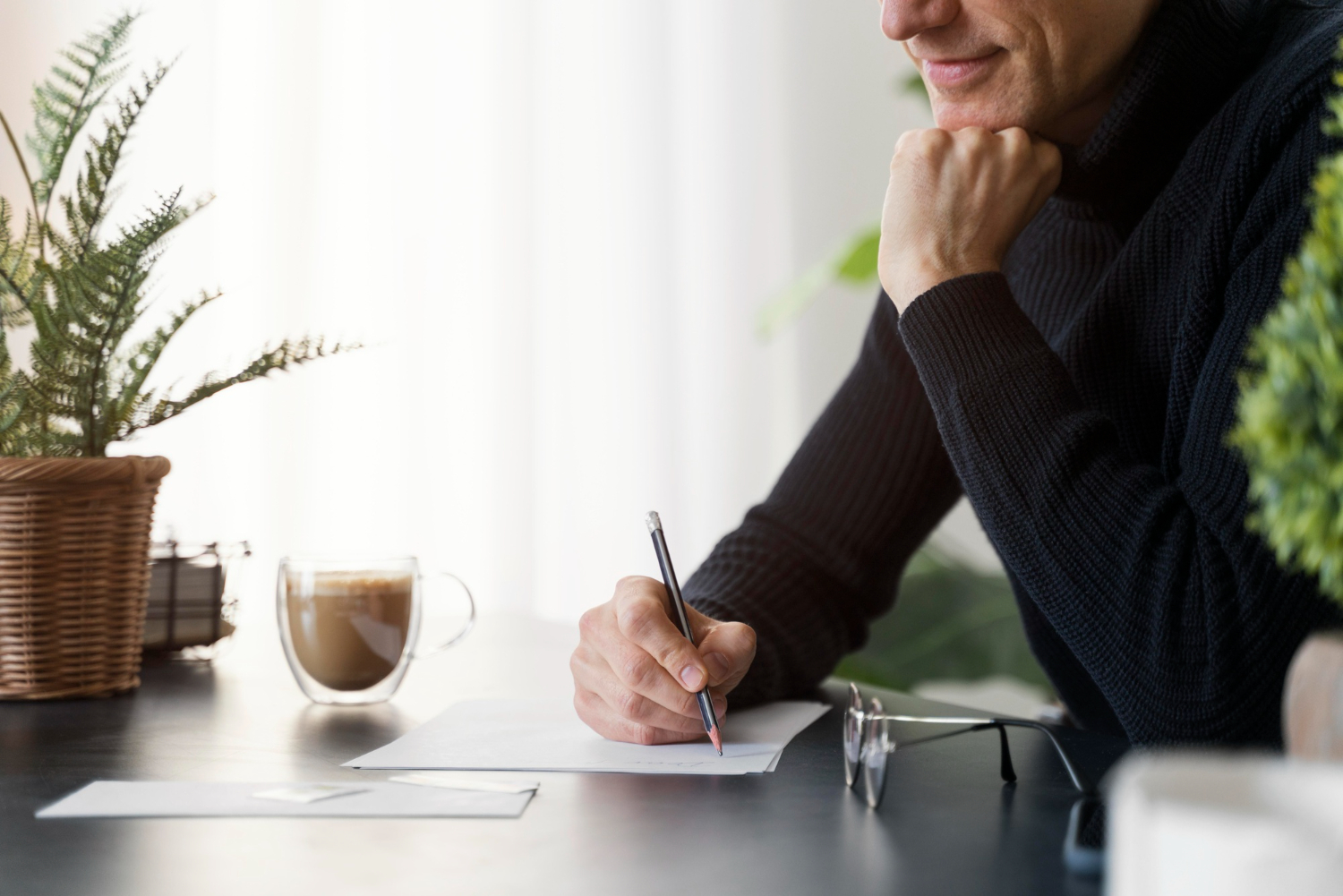 Person writing notes in a Mesa, Arizona law office, surrounded by plants and coffee, reflecting on legal matters.