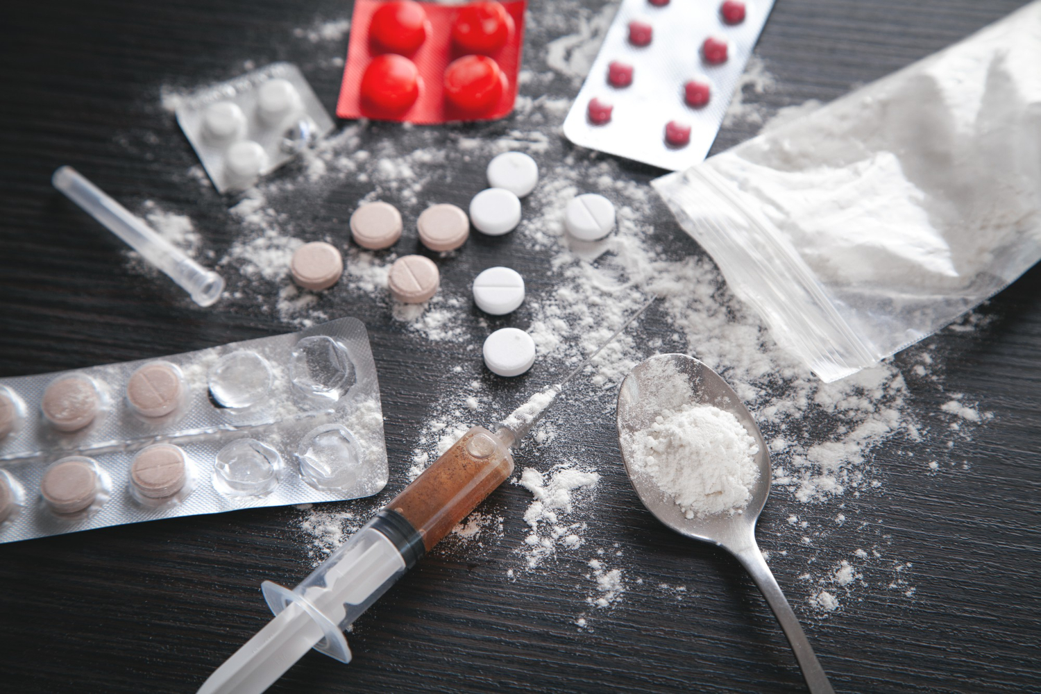 What to Do If You Are Accused of Drug Possession in Arizona Drug paraphernalia including pills, powder, and syringe on a table, illustrating drug possession issues relevant to Arizona law.