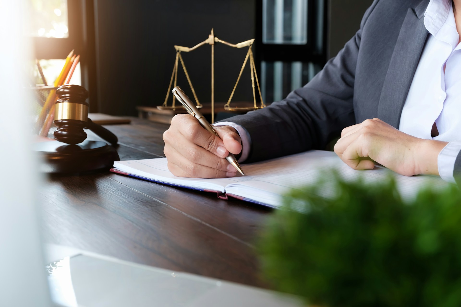 Attorney writing notes in law office with gavel and scales of justice, Mesa, Arizona legal consultation setting.